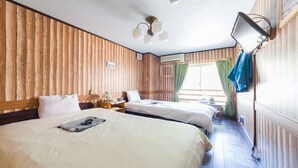 Hotellihuone, jossa on kaksi sänkyä, puupanelointi, kattotuuletin, yöpöytä, lamppu ja ikkuna, jossa on verhot.