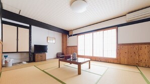 Perinteinen japanilainen huone, jossa on tatamimatto, matala puupöytä, televisio ja suuri ikkuna, josta tulee runsaasti luonnonvaloa.