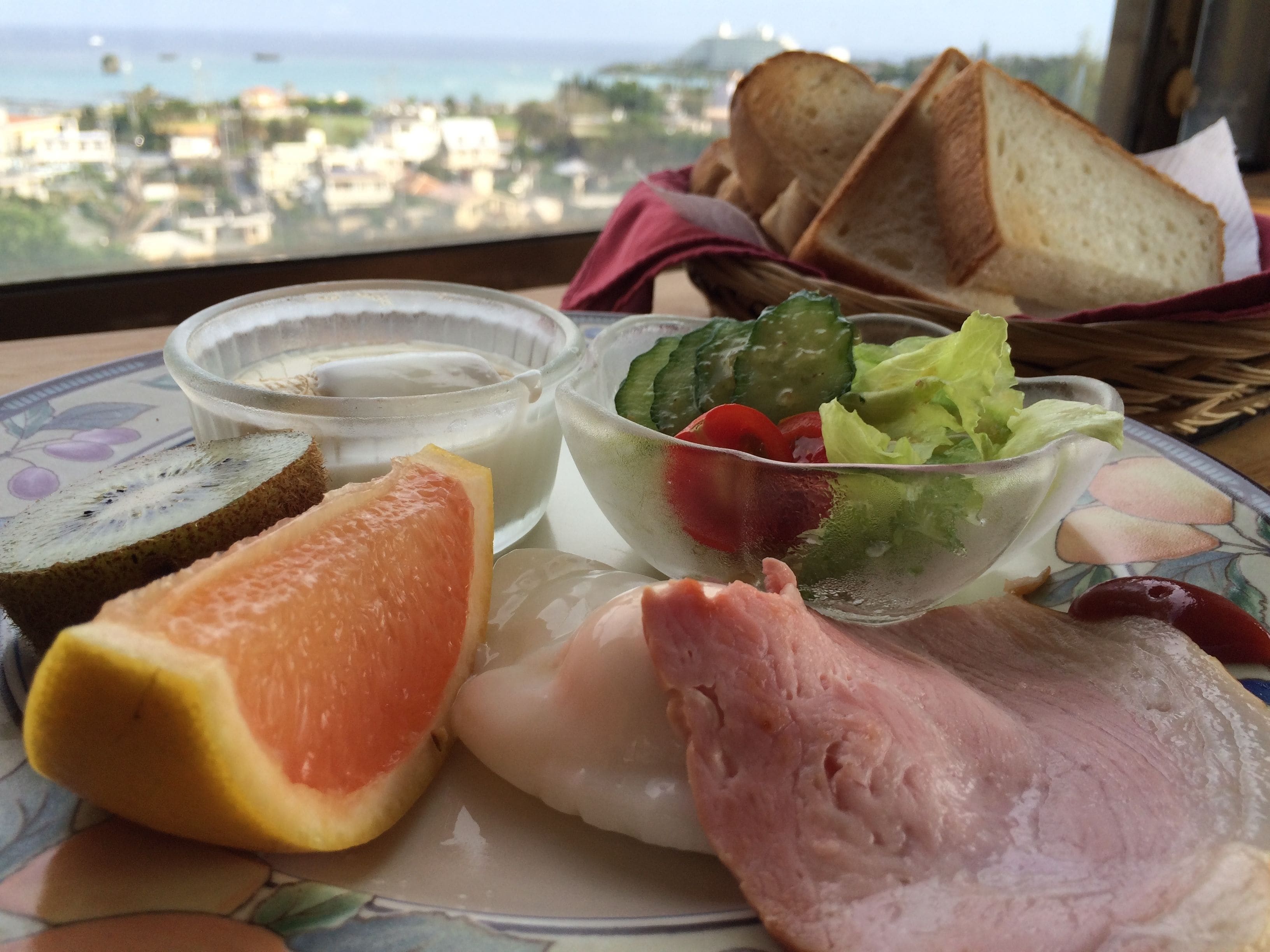 Un plato con pan en rodajas, pomelo, jamón y una ensalada con verduras y un recipiente para aderezo.