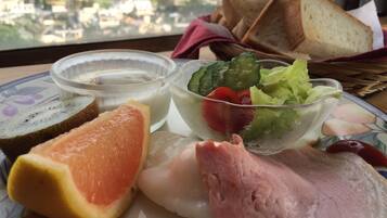 Un plato con pan en rodajas, pomelo, jamón y una ensalada con verduras y un recipiente para aderezo.