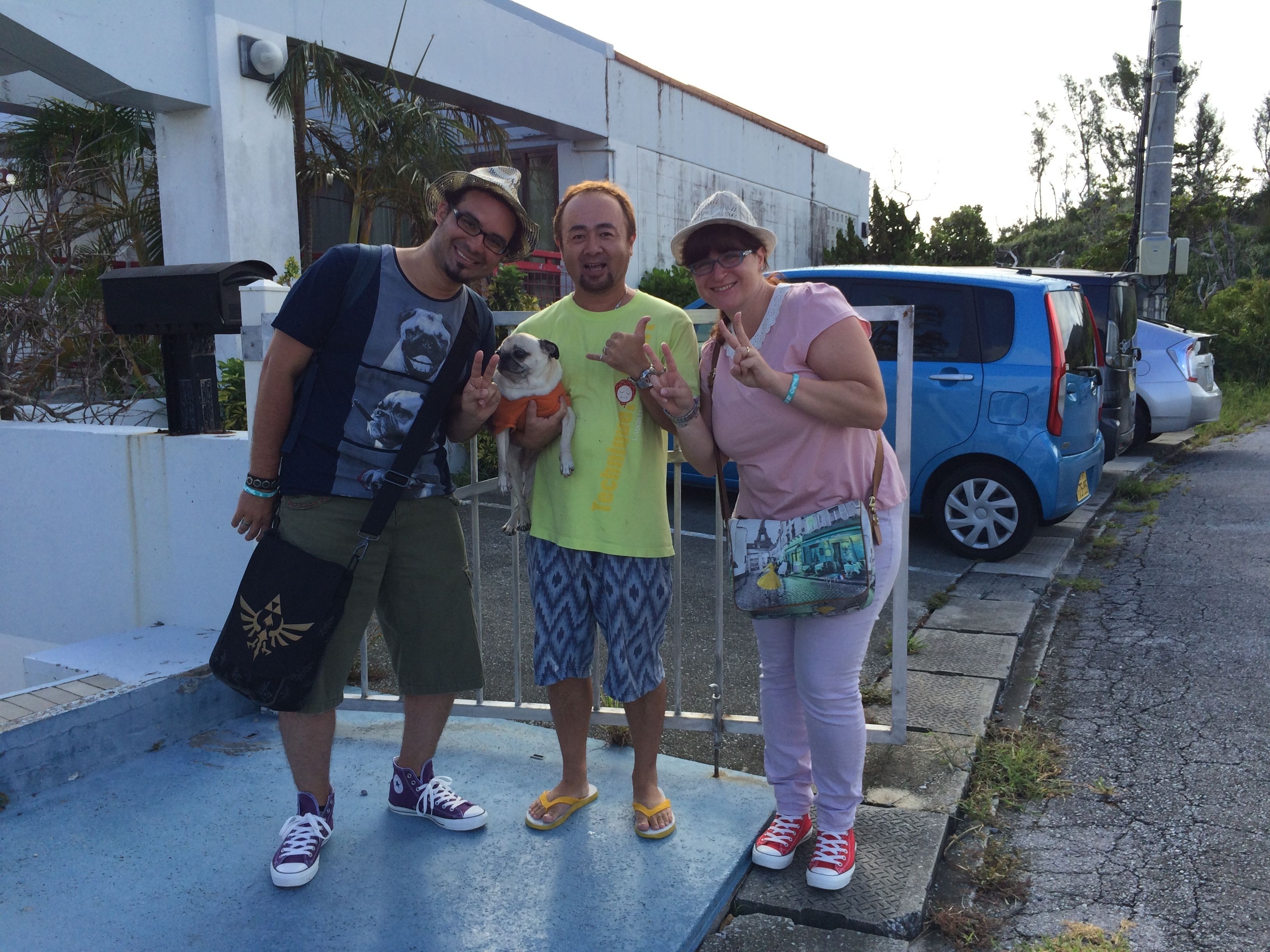 Three people standing on a sidewalk with a blue car parked nearby.
