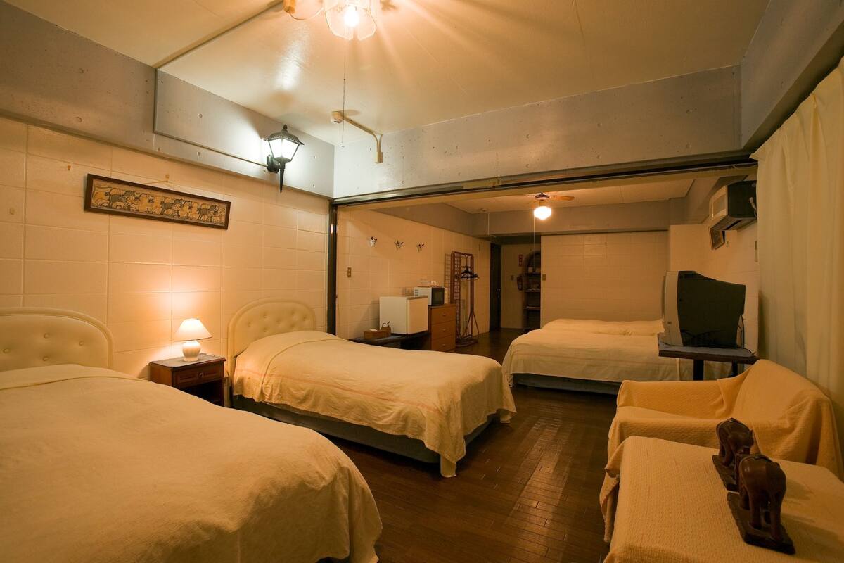 Quarto de hotel com duas camas, uma secretária pequena, uma lâmpada e uma televisão.