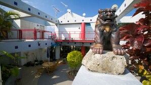 A courtyard with a lion statue on a rock, surrounded by potted plants and outdoor furniture. - Surfside Bed & Breakfast (Onna)