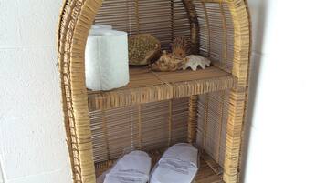A wicker shelf with a rolled-up towel, a decorative shell, and two packages labeled "SLIPPERS for Guests".