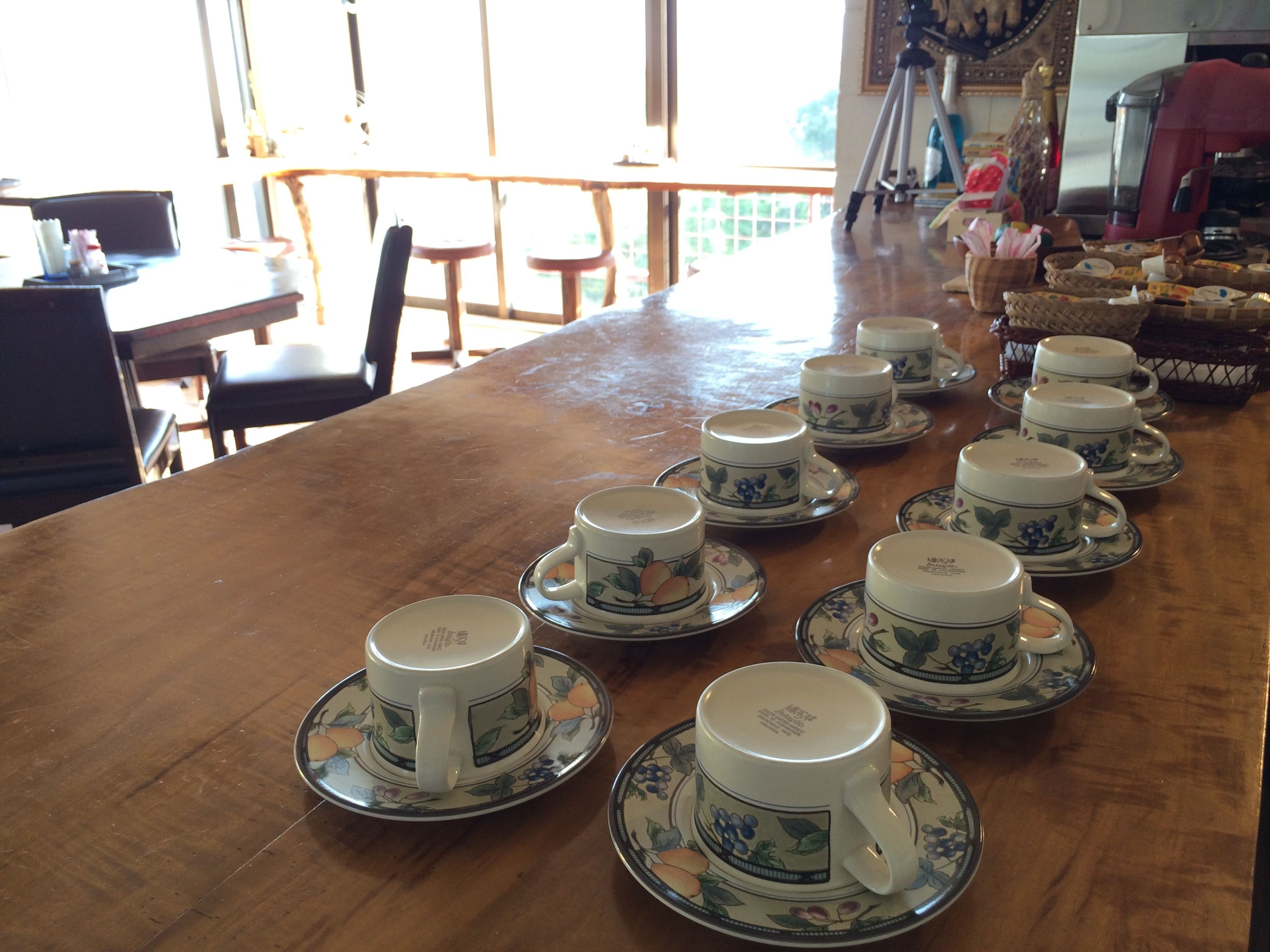 A wooden table with several white ceramic cups and saucers arranged on it.