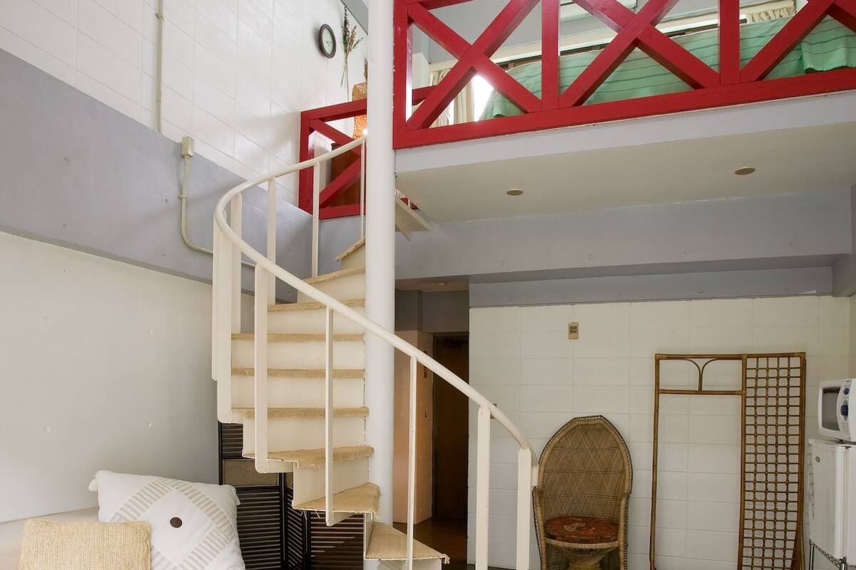Uma sala de estar ampla, com piso de madeira, escada branca, sofá e mesa de centro de vidro.