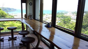 A wooden bar with stools, large windows, and a view of a coastal area. - Surfside Bed & Breakfast (Onna)