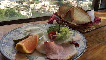 A plate with food items including ham, a slice of orange, and a salad, with a view of buildings and the sea in the background.