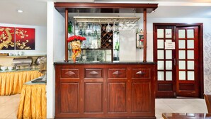 Un comptoir d’accueil en bois avec une vitrine, un espace buffet recouvert d’une nappe jaune et une porte traditionnelle portant le panneau « Interdiction de fumer ».