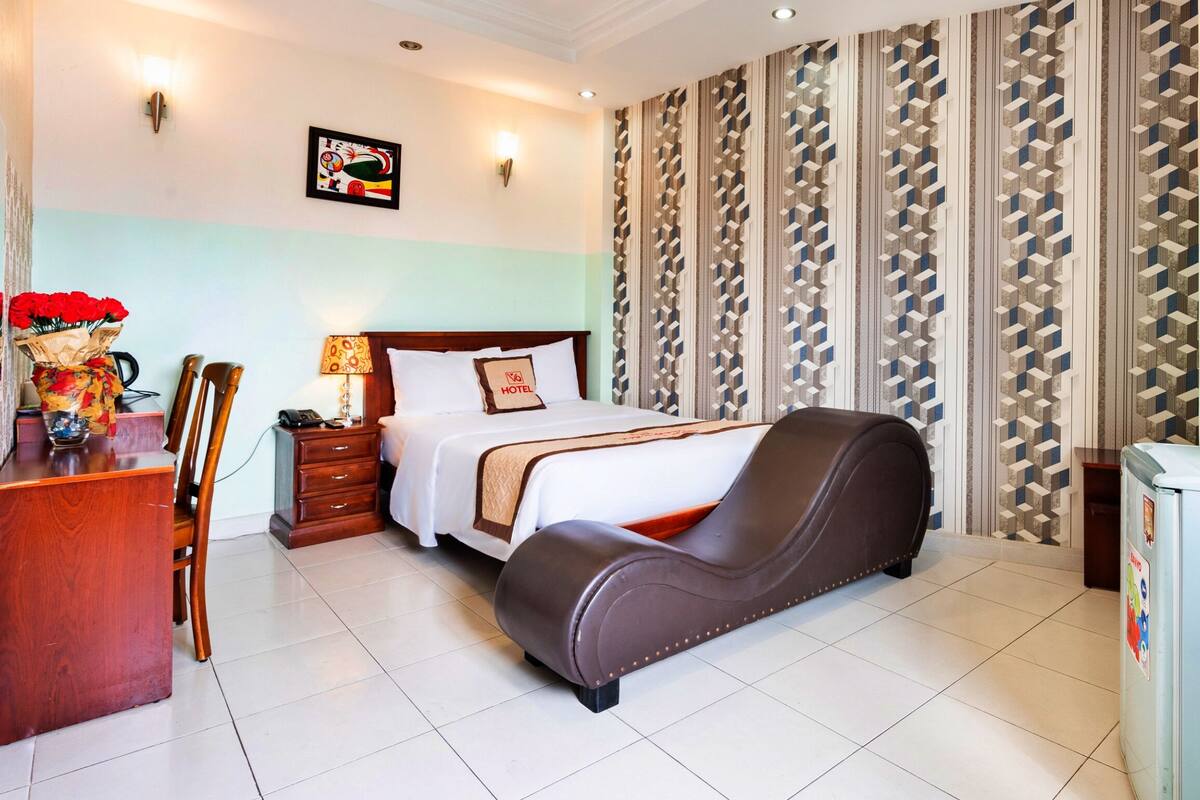 A hotel room with a bed, a desk, a chair, a TV, and a refrigerator.