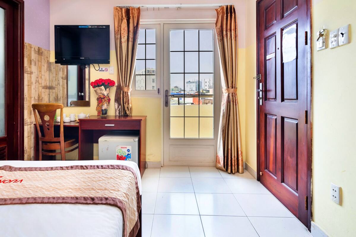 A hotel room with a bed, a desk with a TV, a refrigerator, and a window with curtains.
