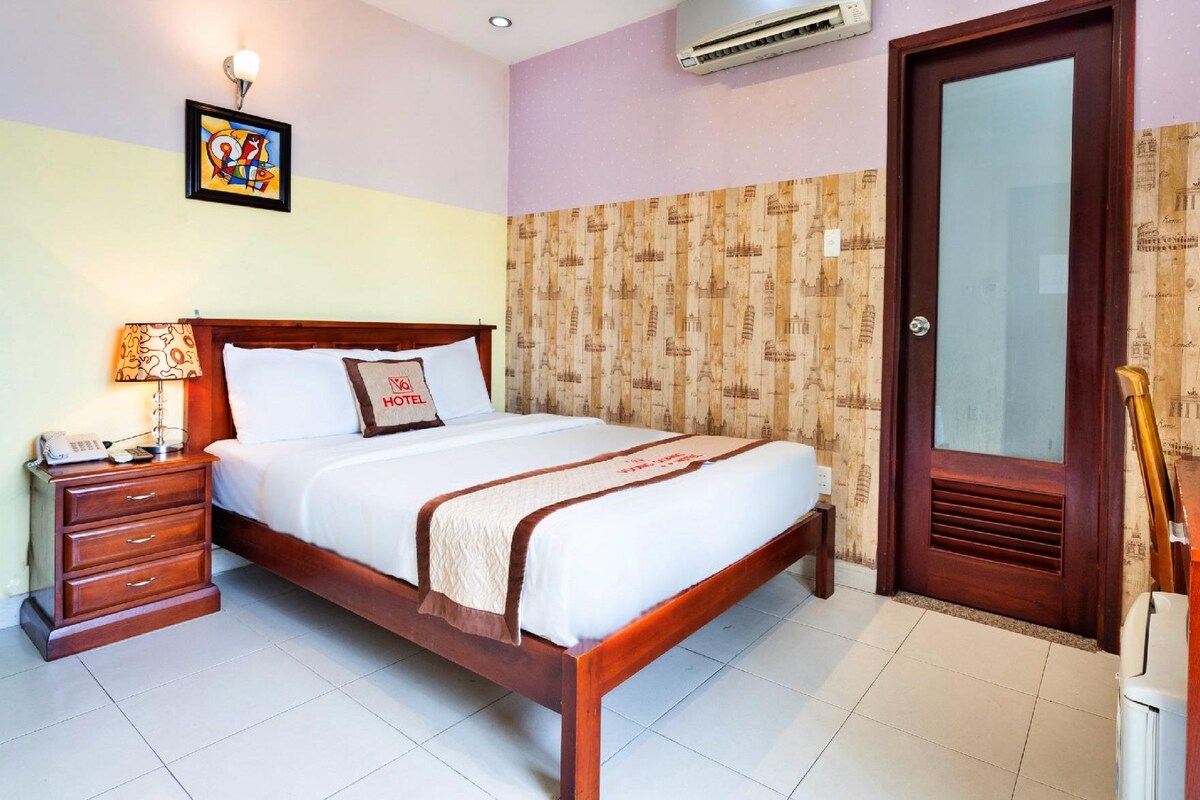 Una habitación de hotel con cama, mesita de noche, lámpara, unidad de aire acondicionado y puerta de madera.