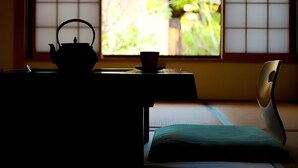 Una habitación japonesa tradicional con suelo de tatami, un juego de té y vistas a la vegetación a través de biombos shoji.
