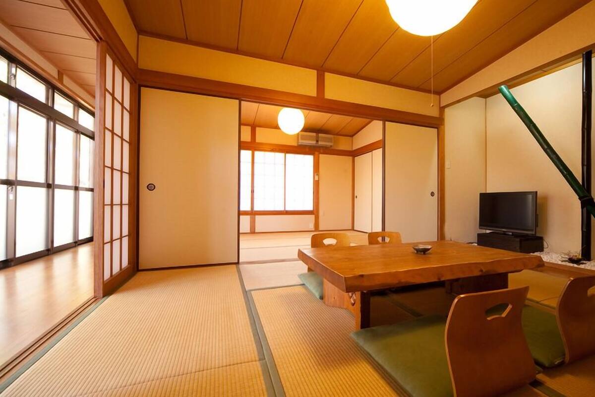 A traditional Japanese room with tatami flooring, a low table, chairs, a television, and sliding doors.