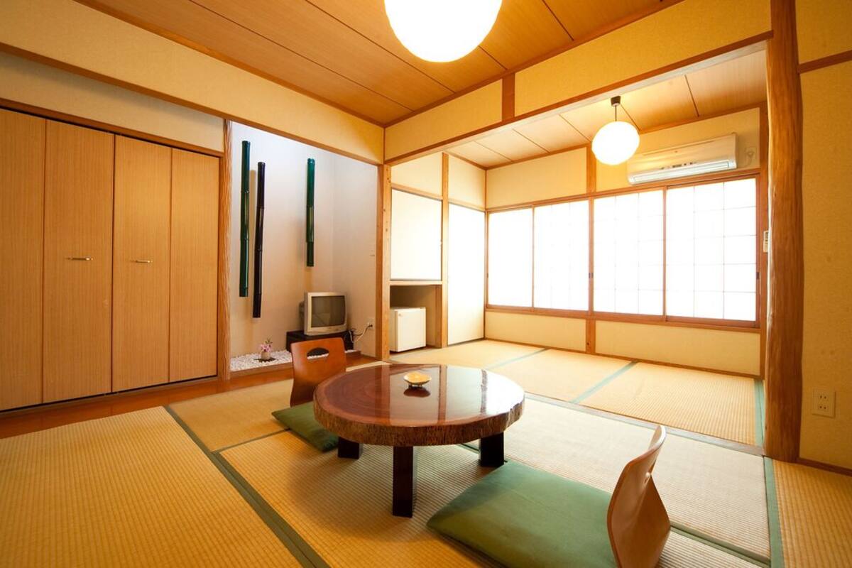 A traditional Japanese room with tatami flooring, a tatami mat table, a television, and sliding doors.