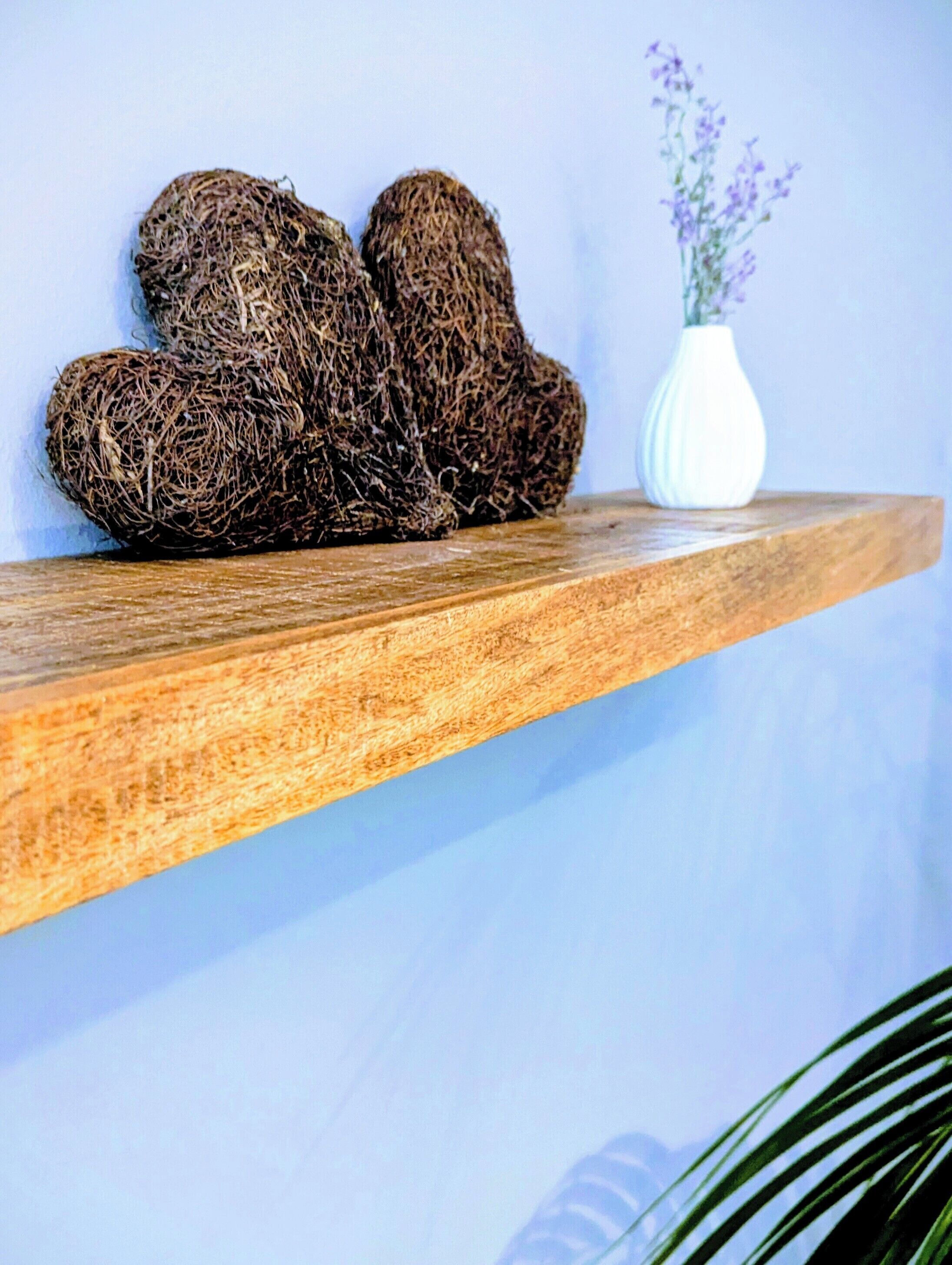 Een houten plank met drie bolvormige objecten en een witte vaas met paarse bloemen.