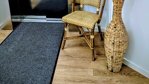 A wooden chair, a woven vase with dried plants, and a black doormat in an elevator. - Hotel Herian (Vaterstetten)