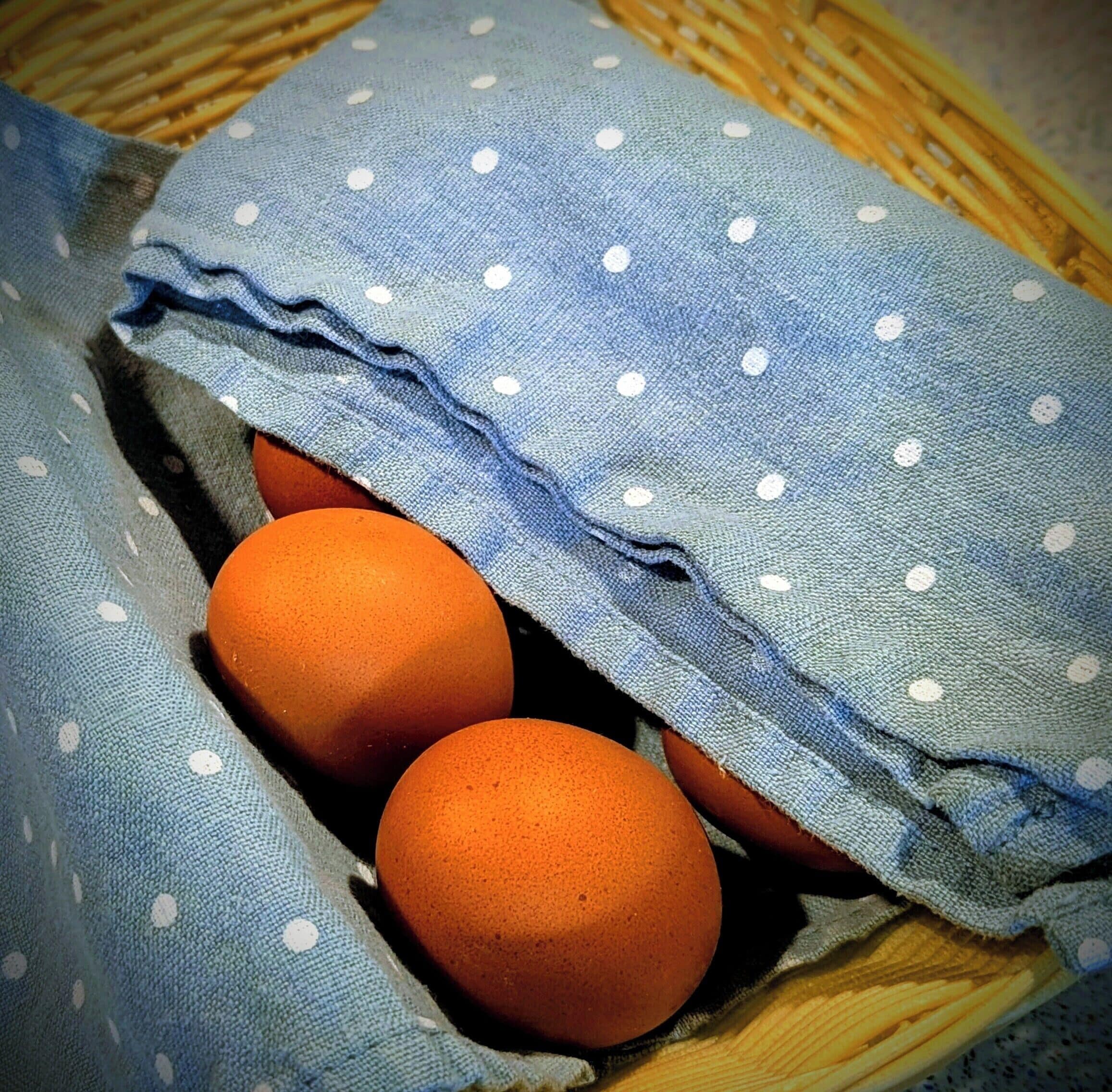 En kurv med to æg, delvist dækket af et blåt stof med prikker.