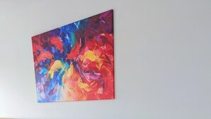 A hotel room with two beds, a wooden headboard, a colorful abstract painting, a bedside lamp, and a power outlet. - Hotel Herian (Vaterstetten)