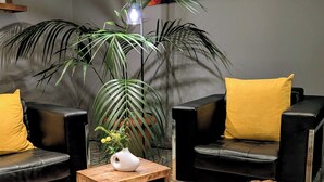 A modern living room with a black leather sofa, wooden coffee table, and two round stools with furry seats. - Hotel Herian (Vaterstetten)