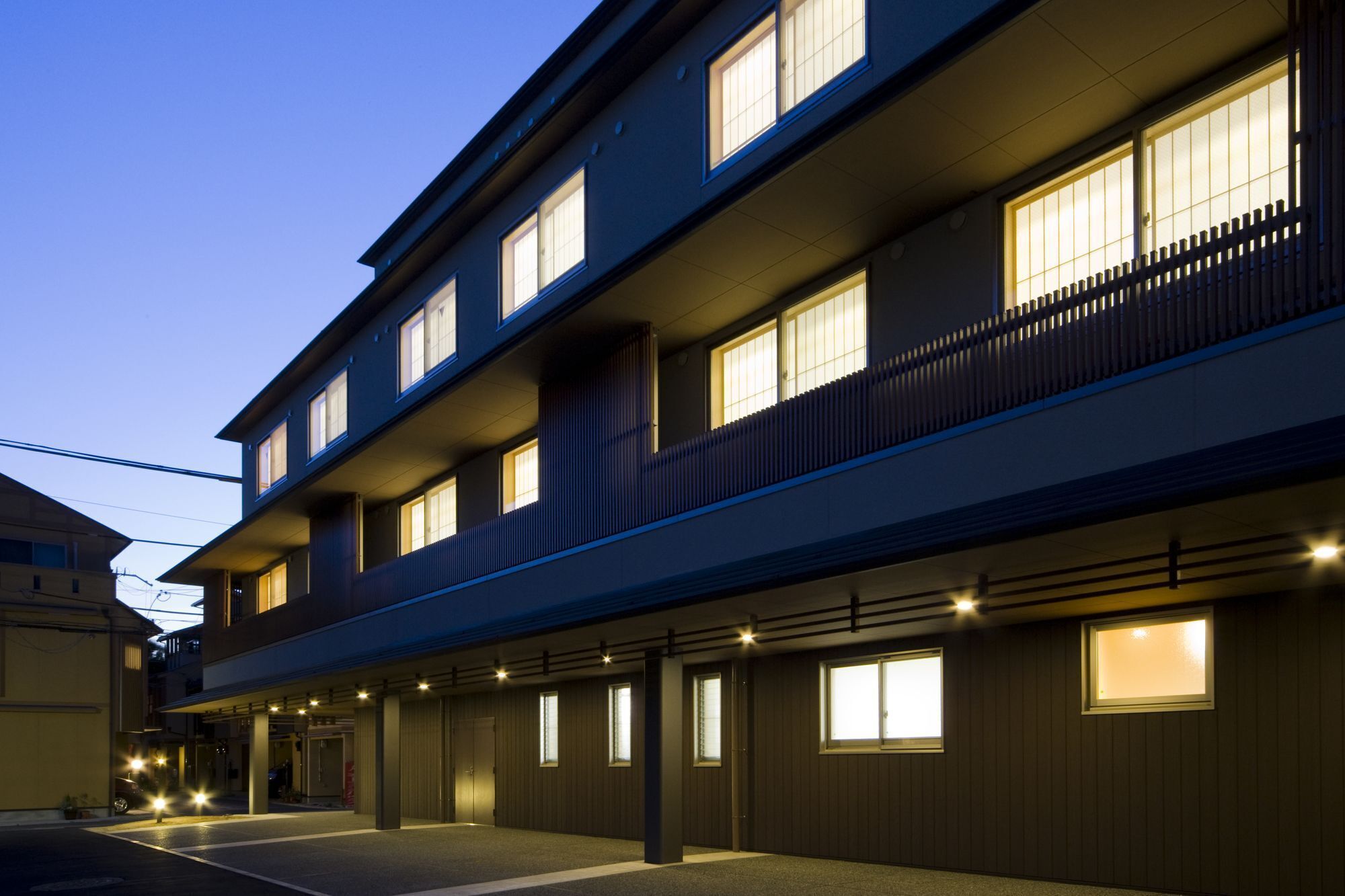 A multi-story hotel with a row of rooms on the ground floor, each with a window and a door.