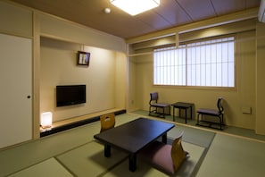 Une pièce de style japonais traditionnel, avec un sol recouvert de tatamis, une table basse, deux chaises, un téléviseur et une fenêtre dotée de panneaux coulissants en papier.