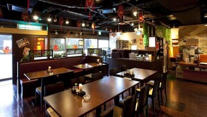 Een restaurantinterieur met houten tafels en zitjes, decoraties en een bakstenen muur.
