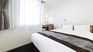 Hotelkamer met een groot bed, een bureau en een stoel. Er is een raam met gordijnen, een spiegel en een lamp aan het plafond.