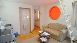 A room with a kitchenette, a sofa, a coffee table, a ladder, and a door with a notice. - BK Weekly Mansion & Hotel (WAKAYAMA SHI)