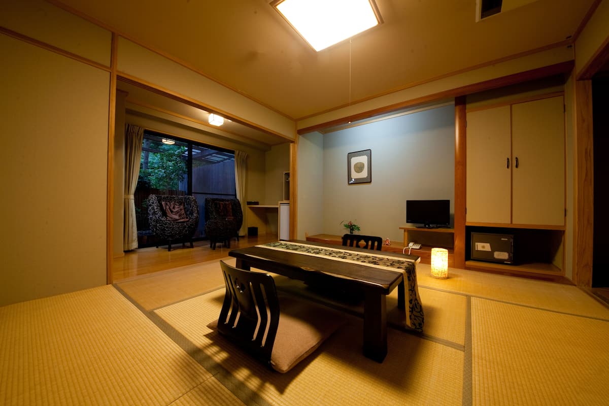 A traditional Japanese room with tatami flooring, a low table, chairs, a television, and sliding doors.