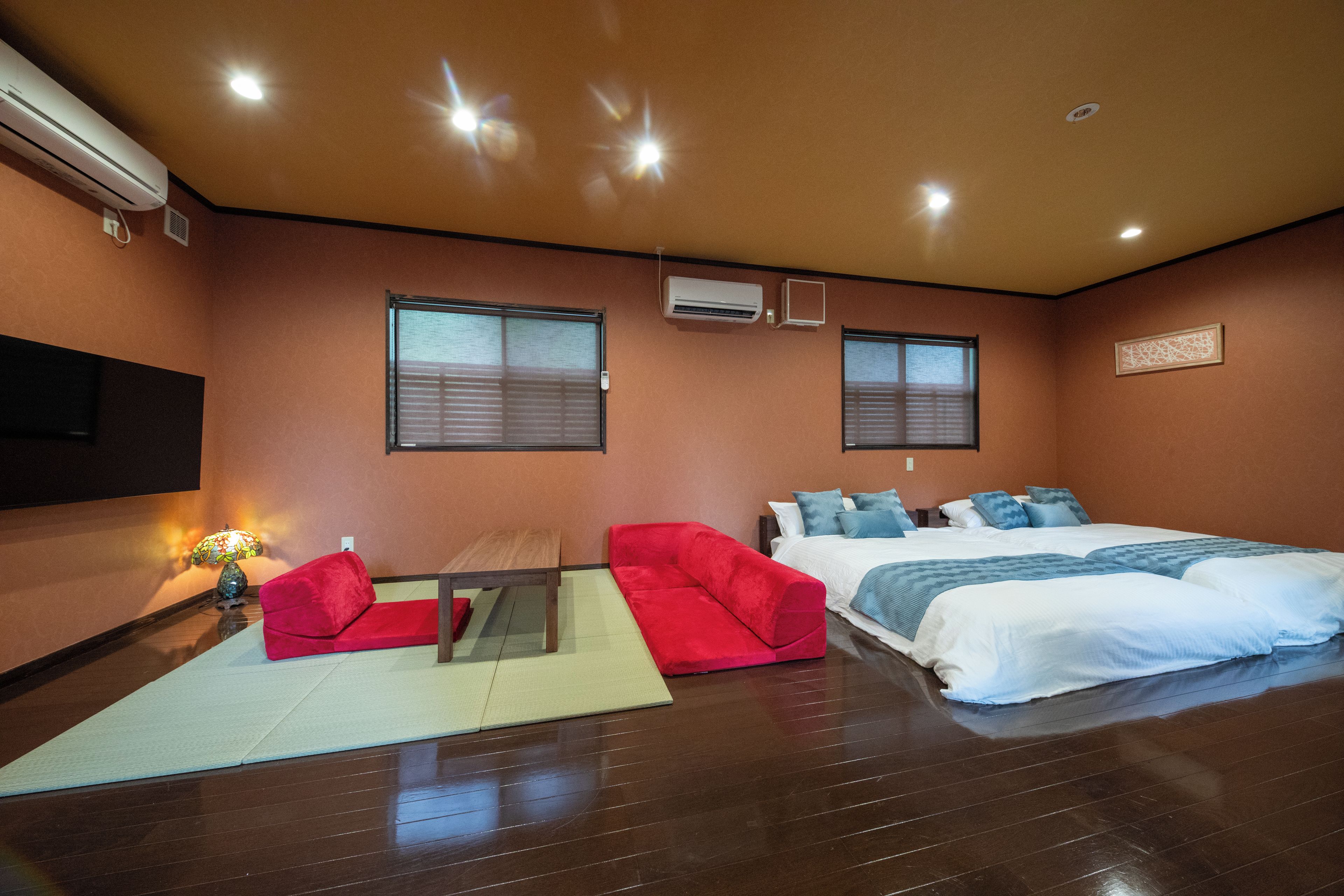 A hotel room with a bed, a desk, two chairs, a lamp, and two windows.