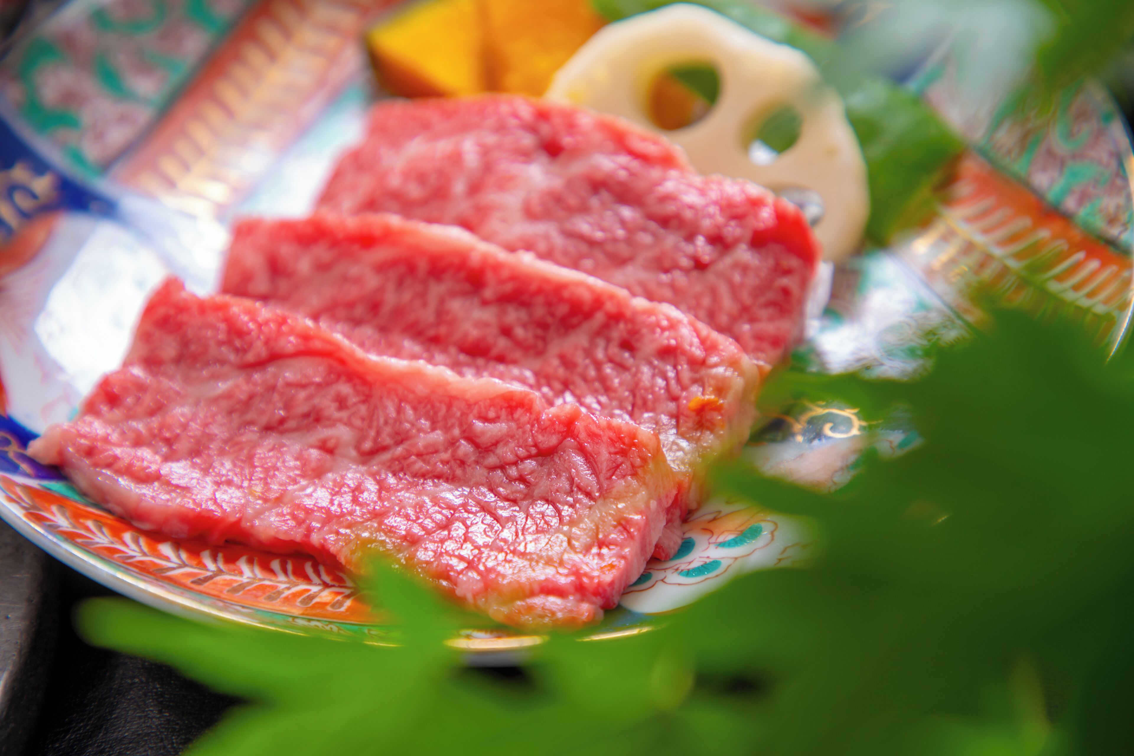 Um prato com fatias de carne crua, uma fruta e um prato decorativo.