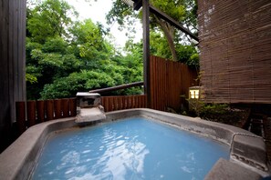 Relax in a serene hot spring area surrounded by lush greenery and a wooden pergola.