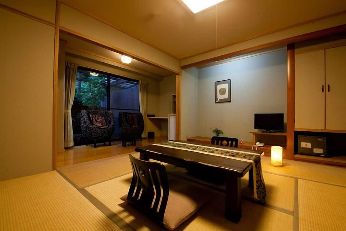Una habitación japonesa tradicional con suelo de tatami, una mesa baja, sillas, un televisor y un armario.