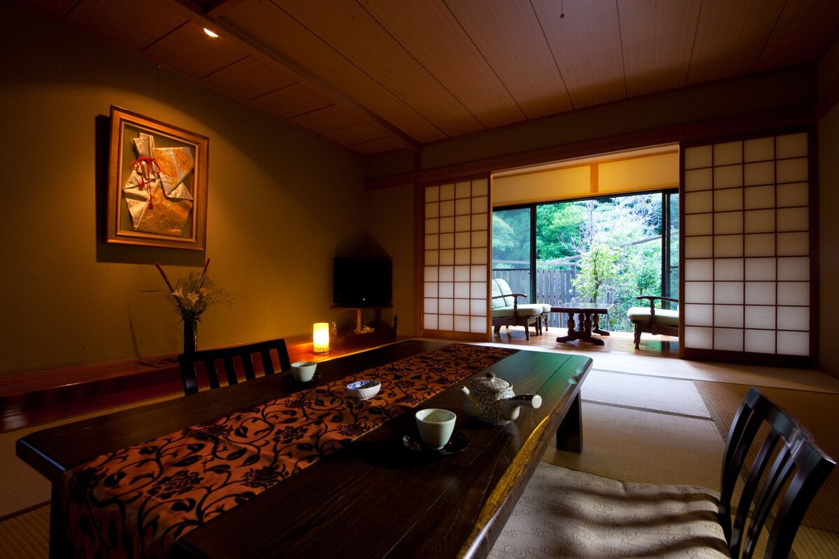 A traditional Japanese room with tatami flooring, a low table with a patterned runner, a tea set, and a sliding shoji screen.