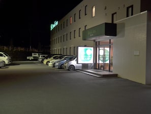 A hotel with a sign reading "Good Inn Hayato" and a large illuminated advertisement. There are several cars parked in front. - Good Inn Hayato (Kirishima)