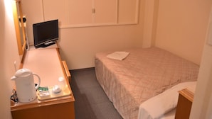 Et lille hotelværelse med seng, skrivebord med elkedel, fjernsyn og garderobeskab.