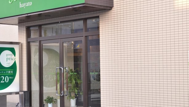 En hotelindgang med et grønt skilt, der siger "good inn hayato", og et skilt, der reklamerer for "good price single room".