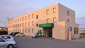 En bygning med et grønt skilt, der viser "Good Inn hayato", og en Coca-Cola automat.