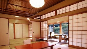 Ett traditionellt japanskt rum med tatamimattor på golvet, ett lågt träbord och en skjutdörr som leder ut till en balkong med utsikt över grönskan.