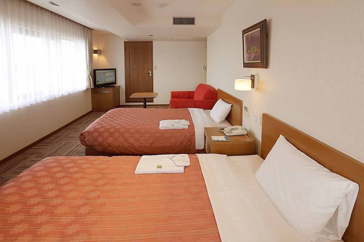 A hotel room with two beds, a TV, a desk, and a red chair.