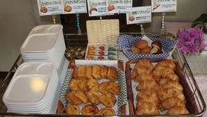 Un bufé con una variedad de productos de pastelería y panadería, incluyendo croissants y panes, exhibidos en cestas y bandejas.