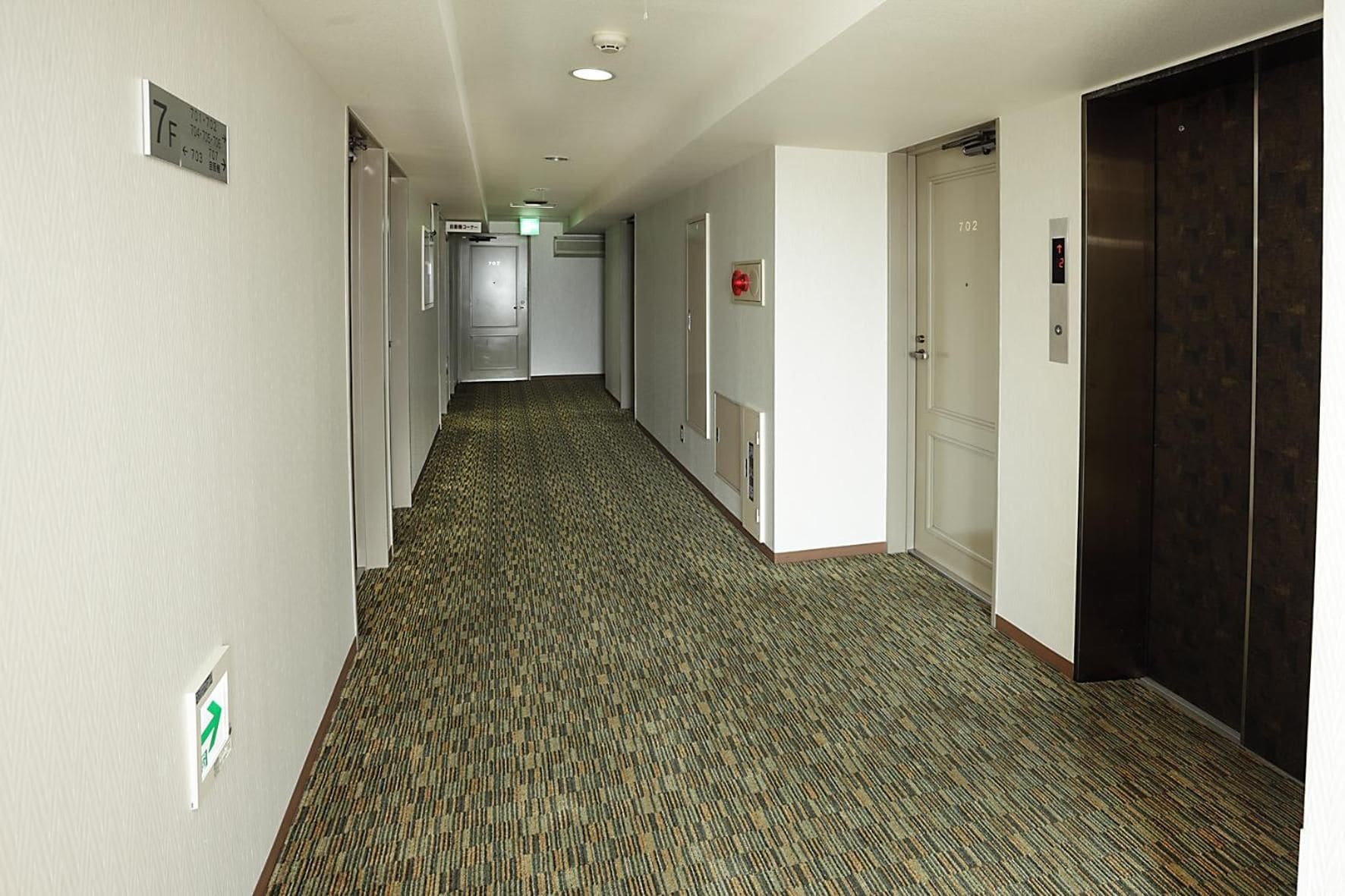 A hotel hallway with carpeted floors, doors, and an elevator.