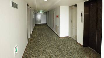 A hotel hallway with carpeted floors, doors, and an elevator.