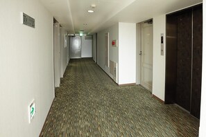 A hotel hallway with carpeted floors, doors, and an elevator. - Kumegawa Wing Hotel (Higashimurayama)