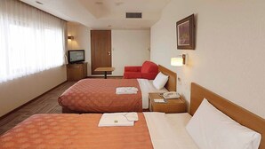 Habitación de hotel con dos camas, televisión, escritorio, silla y sofá rojo.