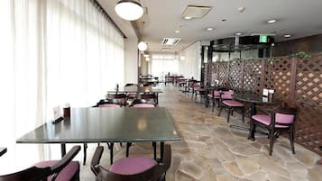A restaurant with tables and chairs, a stone floor, and a view through a window with curtains.