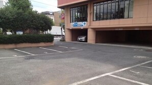 Un estacionamiento con espacios delimitados, entrada a un edificio y señalización de dirección.