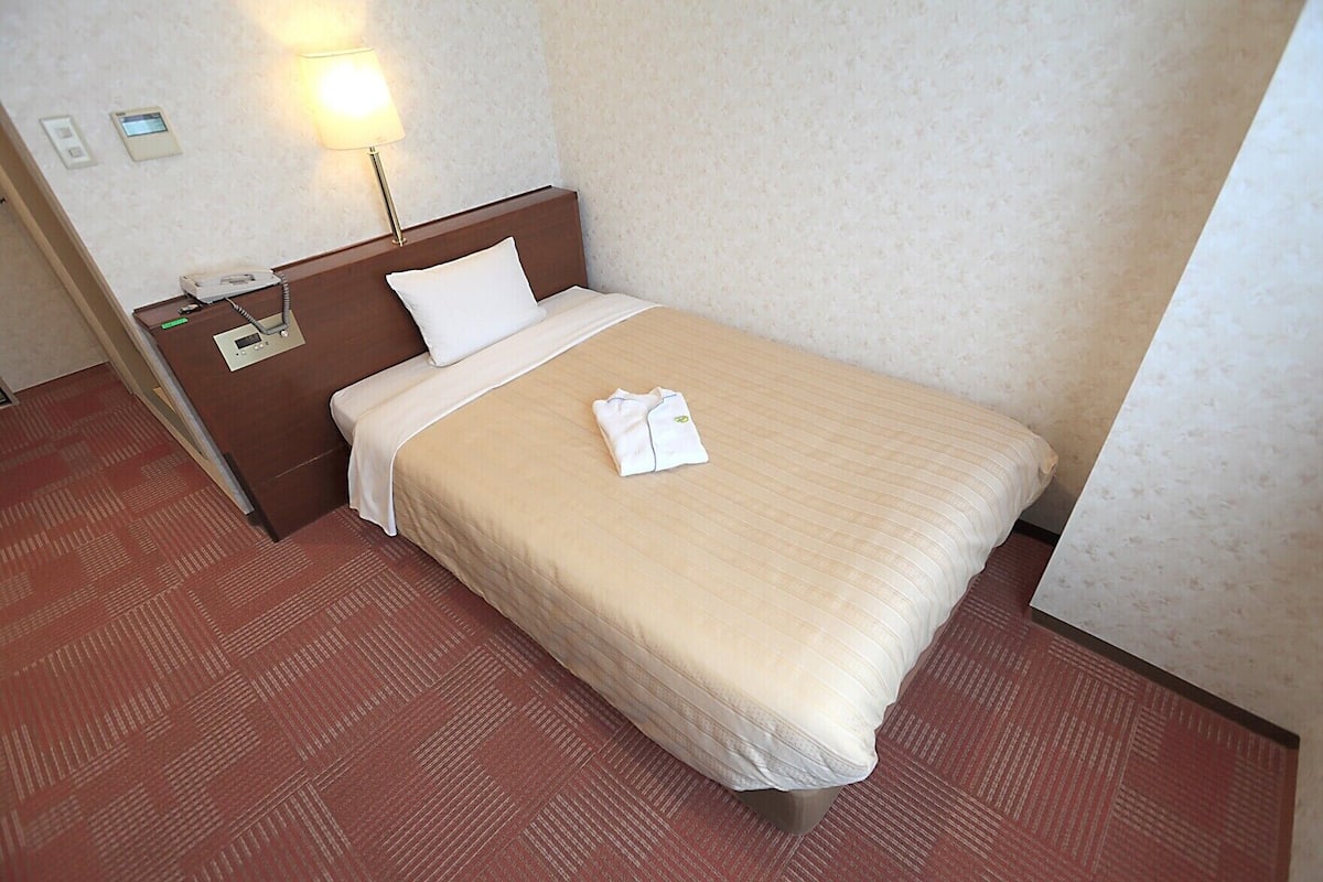 A hotel room with a bed, a nightstand, a lamp, and a telephone.