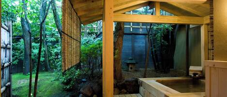 A wooden structure with a hot spring area, surrounded by trees and a garden.